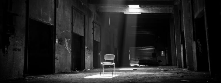 A dark warehouse with a chair being illuminated from above