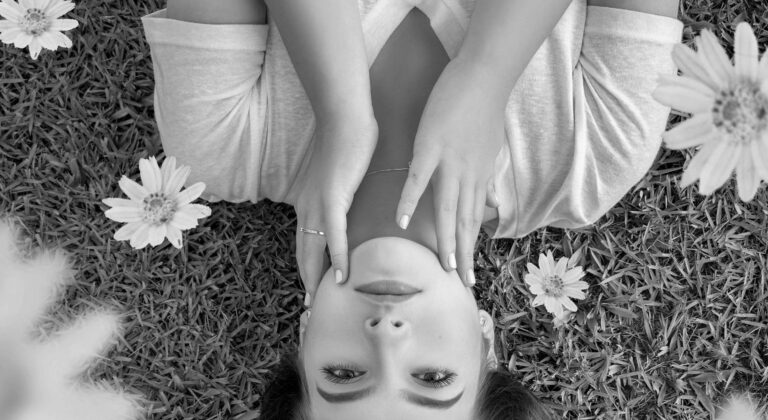 Black and white image of a woman laying on the grass surrounded by flowers