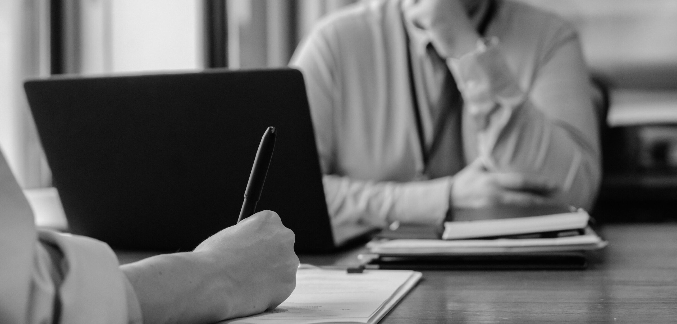 Blurred photo of a man writing on a clipboard on his desk while an employee sits waiting