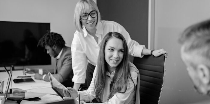 Two office women smiling while looking at a male colleague off-camera